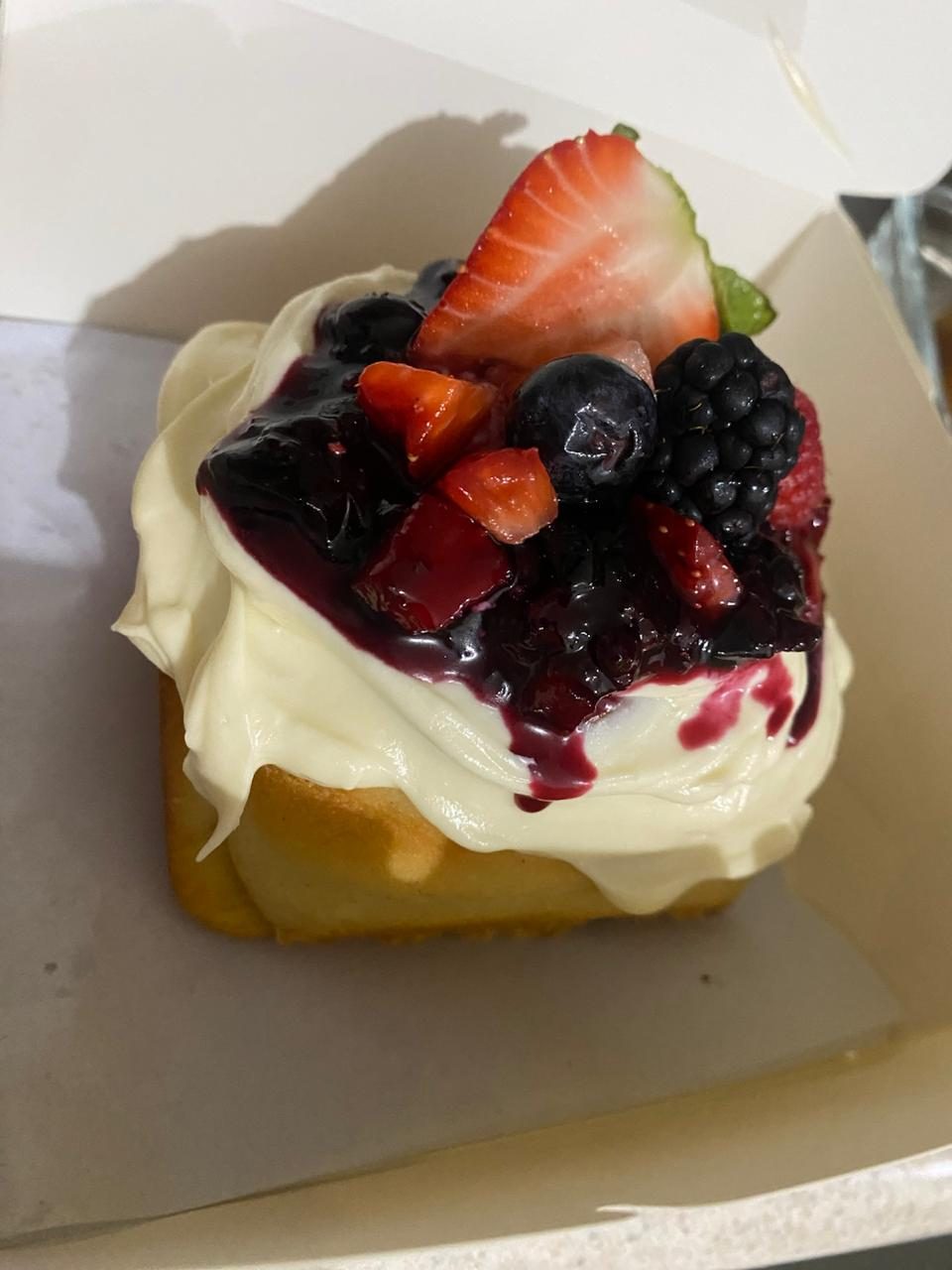 Rol de canela relleno con crema, frutos rojos y una fresa entera encima.